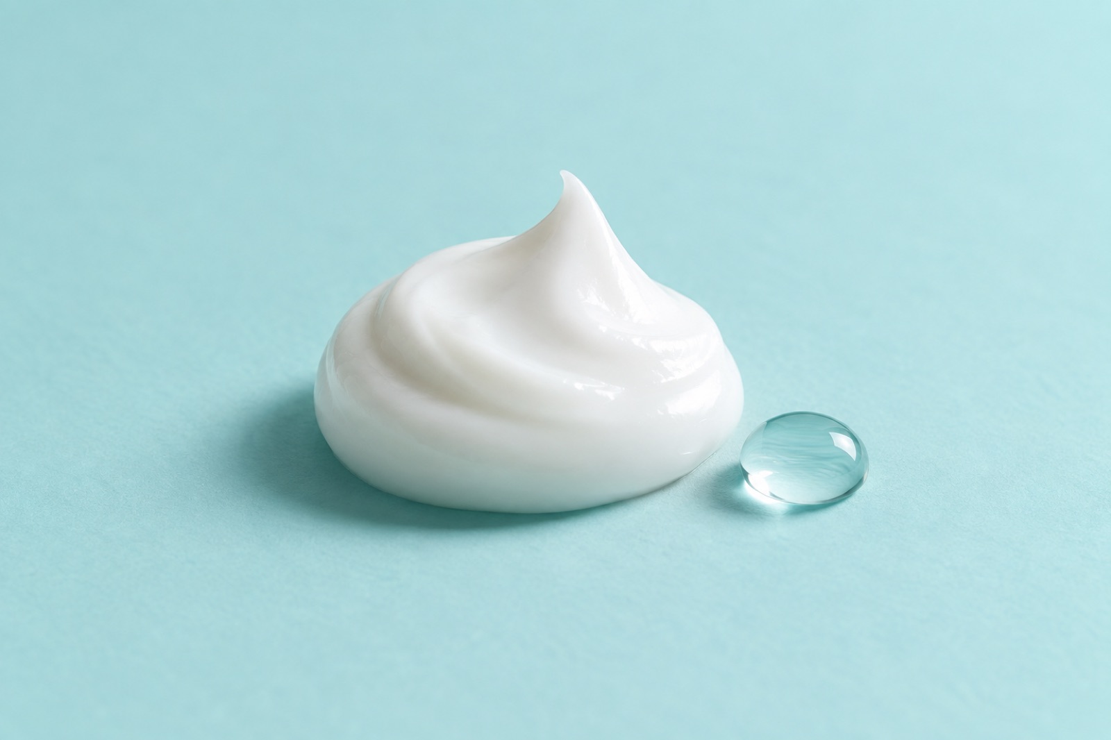 하늘색 바닥 위에 끝이 뾰족하게 솟은 흰 크림 한 덩이와 그 옆에 놓인 작은 투명 물방울 하나