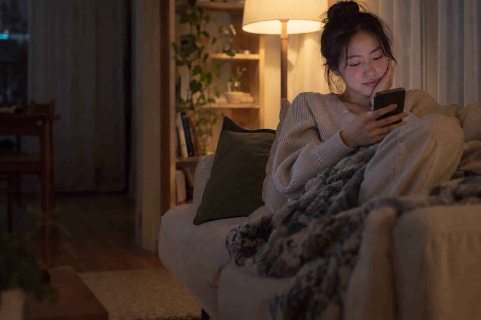 소파에 앉아 한 손은 볼에, 한 손은 휴대폰에 둔 저녁의 20대 여성