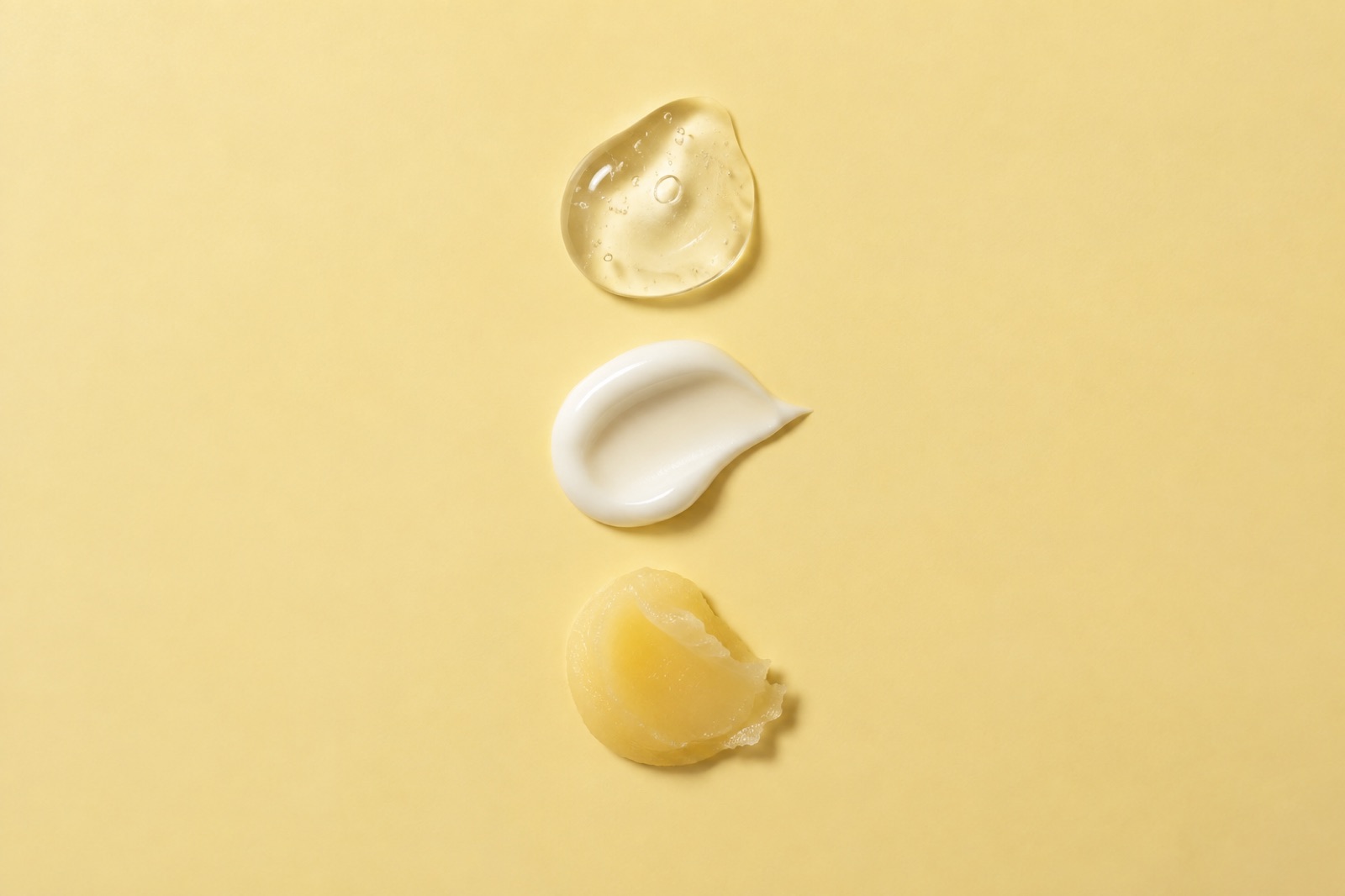 연노랑 바탕에 세로로 놓인 세 가지 제형, 기포가 든 투명한 젤과 윤기 나는 흰 크림, 노르스름하고 된 밤